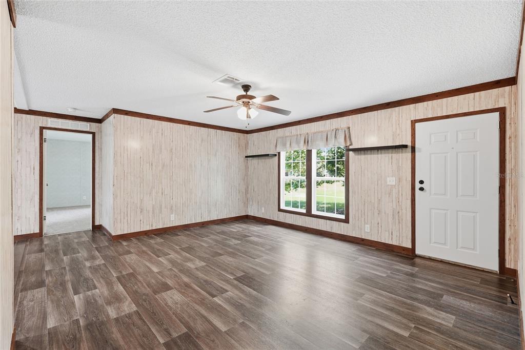 An empty room features wood-look flooring, paneled walls, a ceiling fan, and a white door — 291 SW LEGION DRIVE, LAKE CITY, FL