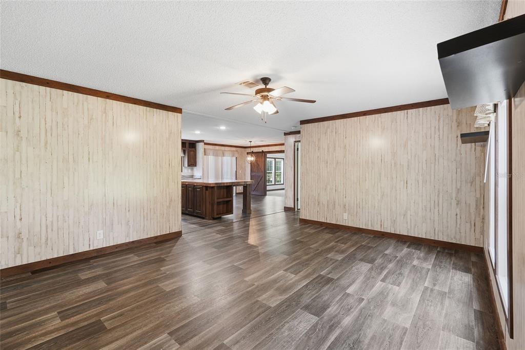 A room with wood-look plank flooring and light-colored vertical paneling leads toward a kitchen area — 291 SW LEGION DRIVE, LAKE CITY, FL