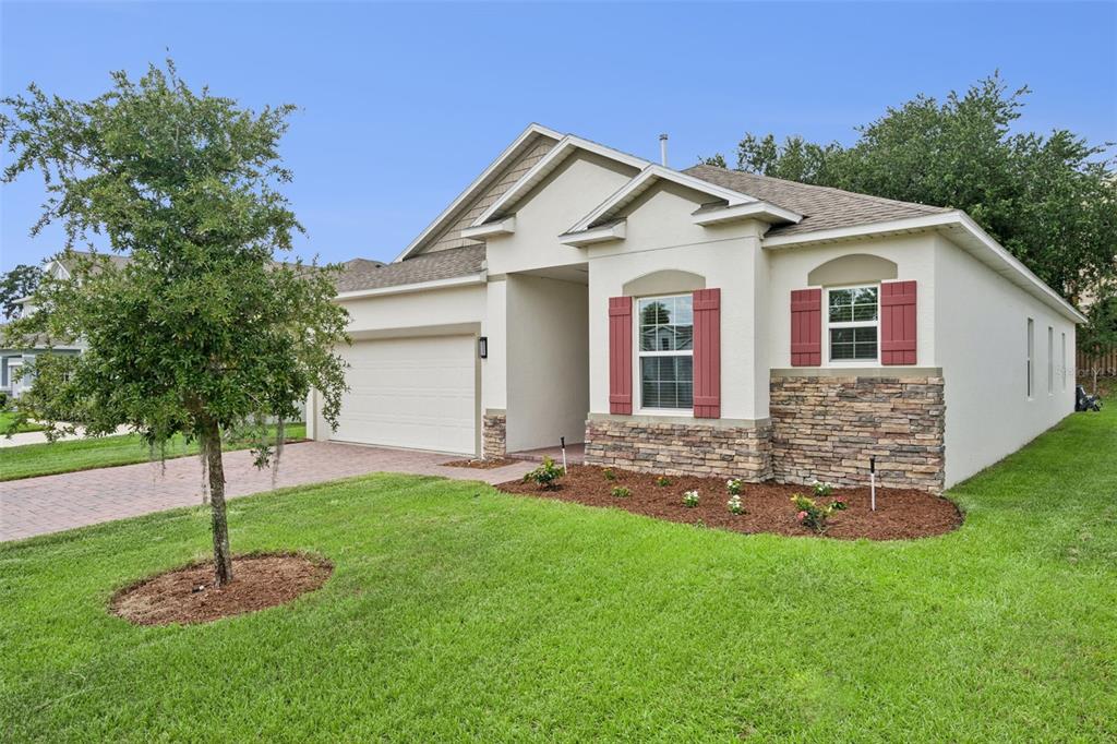 A single-story house with a beige stucco exterior, stone accents, and red window shutters — 1029 BRADFORD RIDGE DRIVE, LEESBURG, FL
