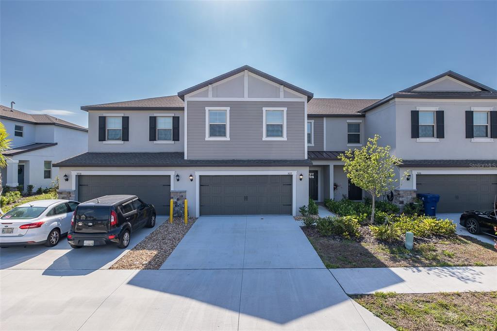 A two-story townhouse exterior features gray siding, a two-car garage, and a concrete driveway — 3072 HOVER HALL LANE, NEW PORT RICHEY, FL