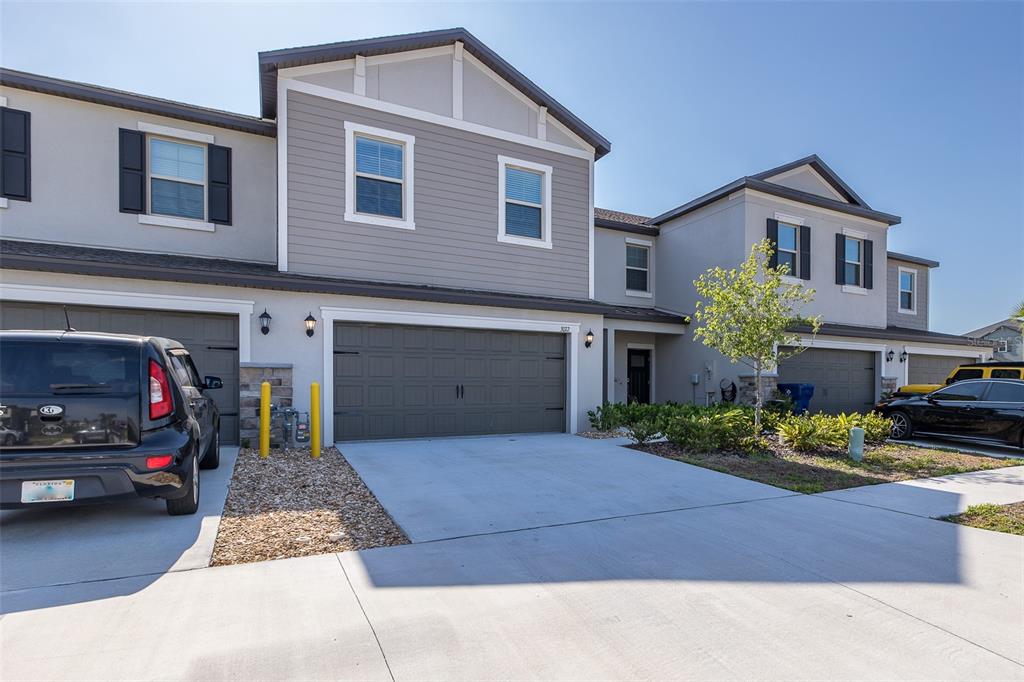A two-story townhouse with a gray garage, beige siding, and a concrete driveway — 3072 HOVER HALL LANE, NEW PORT RICHEY, FL