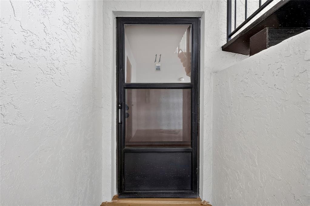A black storm door with glass panels is set into a white stucco entryway — 3272 S SEMORAN BOULEVARD UNIT 11, ORLANDO, FL