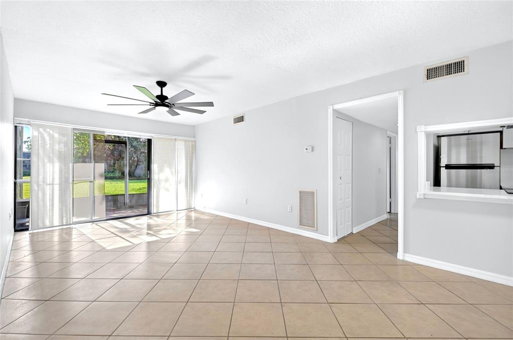 An empty living room features light-colored tile flooring, a ceiling fan, and sliding glass doors — 3272 S SEMORAN BOULEVARD UNIT 11, ORLANDO, FL