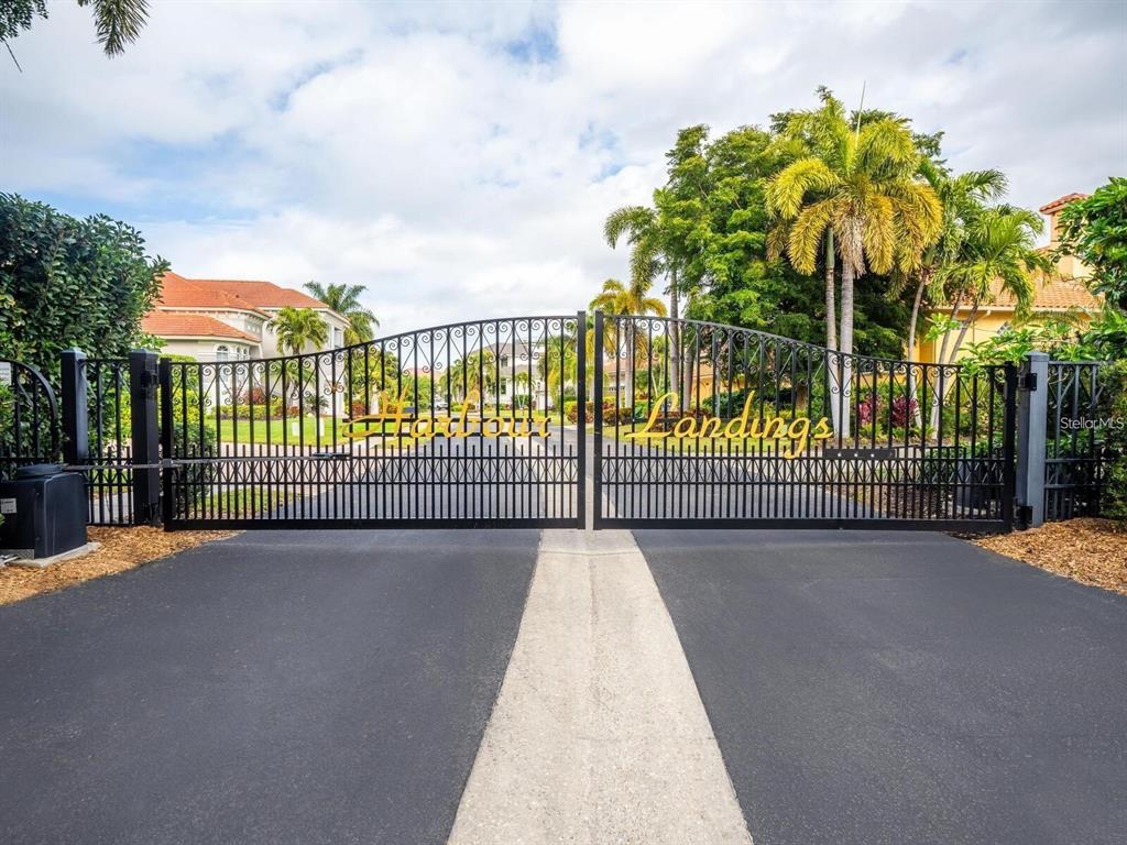 A black metal gate marks the entrance to a residential community with palm trees — 4118 OSPREY HARBOUR LOOP UNIT 4118, CORTEZ, FL