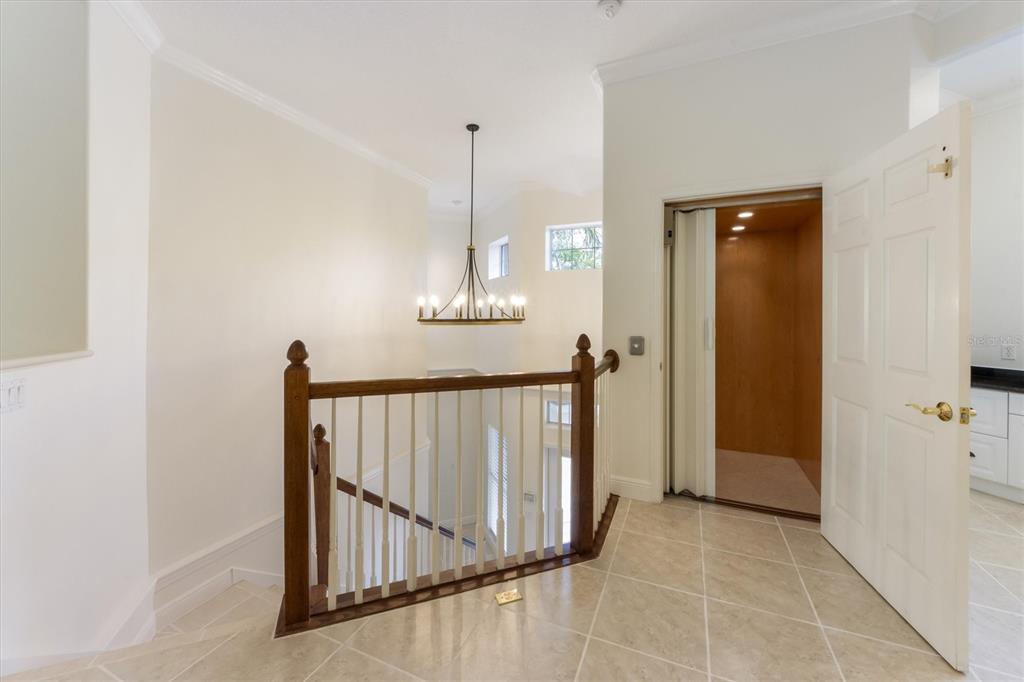 A landing with tile flooring, a wooden staircase railing, a chandelier, and an open elevator — 4118 OSPREY HARBOUR LOOP UNIT 4118, CORTEZ, FL