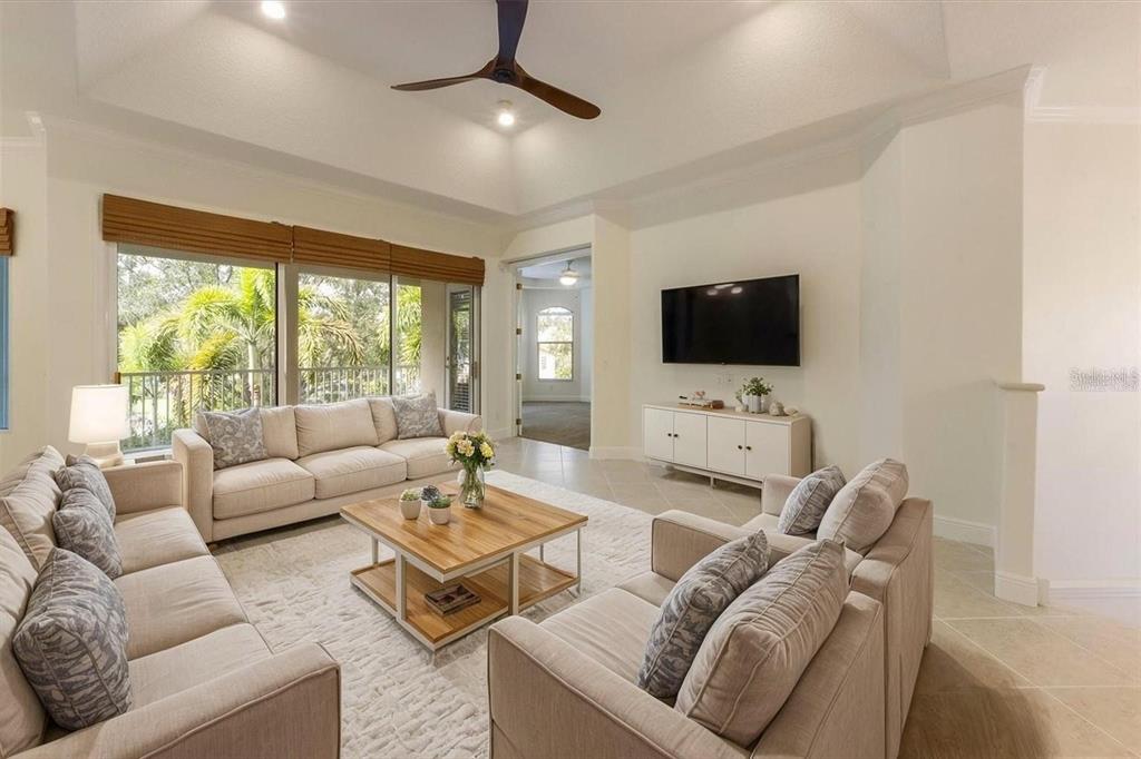 A bright living room features a tray ceiling, beige sofas, a wooden coffee table, and television — 4118 OSPREY HARBOUR LOOP UNIT 4118, CORTEZ, FL