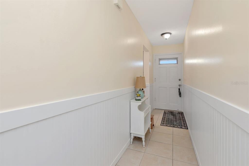 A narrow entryway features light-colored walls with white wainscoting, tile flooring, and a white door — 3128 59TH STREET S UNIT 211, GULFPORT, FL