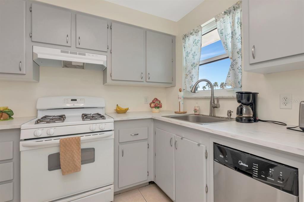 A kitchen features grey cabinets, white countertops, a white gas stove, and a black dishwasher — 3128 59TH STREET S UNIT 211, GULFPORT, FL