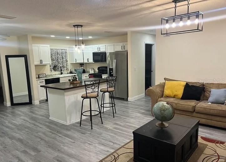 An open-concept kitchen and living area features white cabinets, a breakfast bar, and gray flooring — 1020 LEE AVENUE NW, PALM BAY, FL