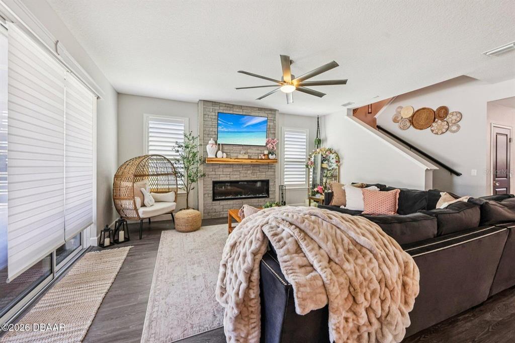 A living room features a stone fireplace, a dark sectional sofa, and a wicker chair — 6827 FORKMEAD LANE, PORT ORANGE, FL