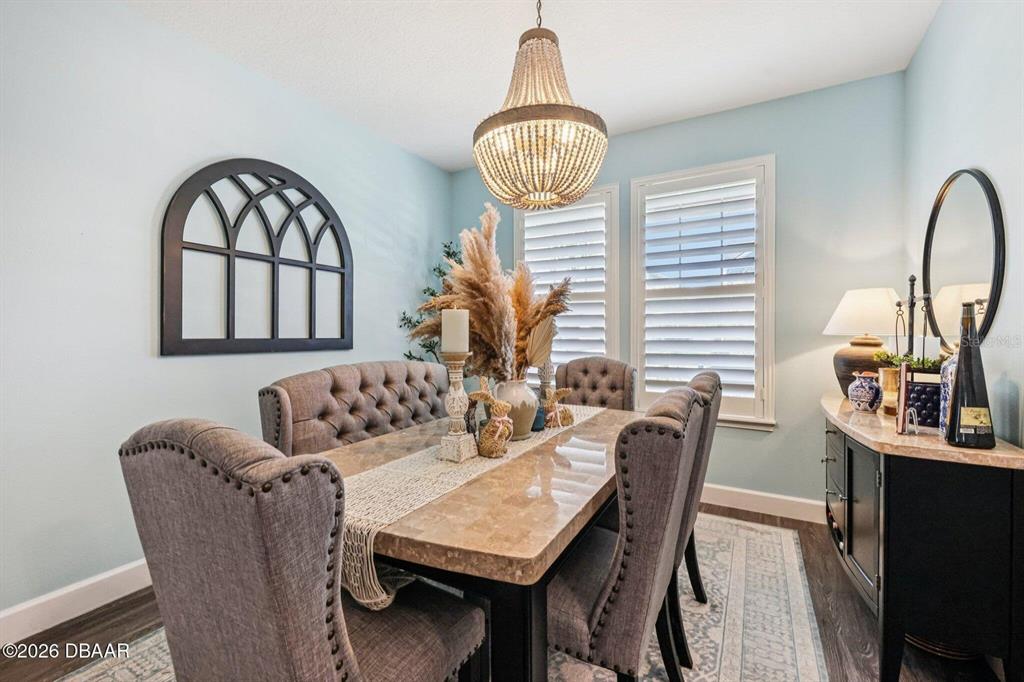 A dining room features a tufted bench, upholstered chairs, a chandelier, and a stone-topped table — 6827 FORKMEAD LANE, PORT ORANGE, FL