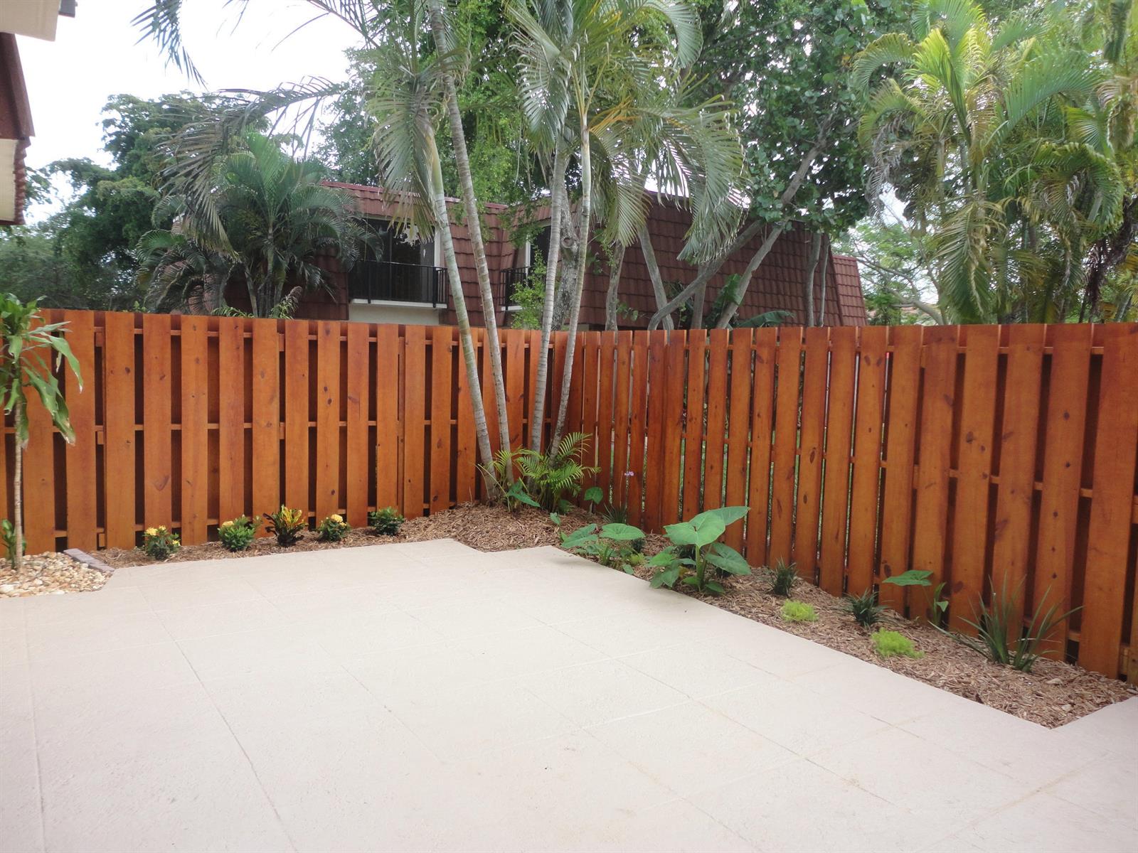 A backyard patio features light-colored pavers, a wood privacy fence, and a landscaped garden bed — 3008 San Clara Drive # b, Delray Beach FL 33445, DELRAY BEACH, FL