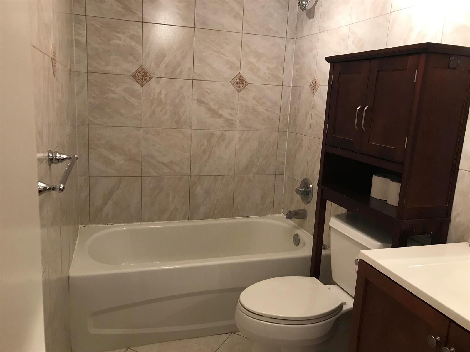 A bathroom features a white bathtub, a toilet with an over-the-toilet cabinet, and tiled walls — 3008 San Clara Drive # b, Delray Beach FL 33445, DELRAY BEACH, FL