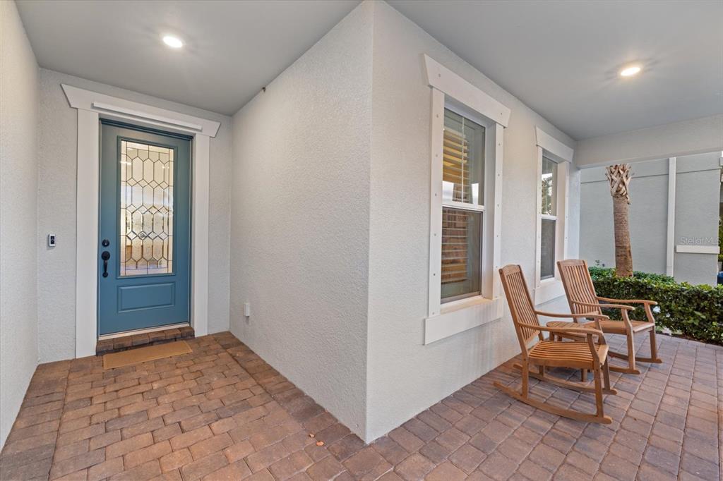 A covered front porch features a blue door, brick pavers, and two wooden rocking chairs — 11712 GOLDEN BAY PLACE, BRADENTON, FL
