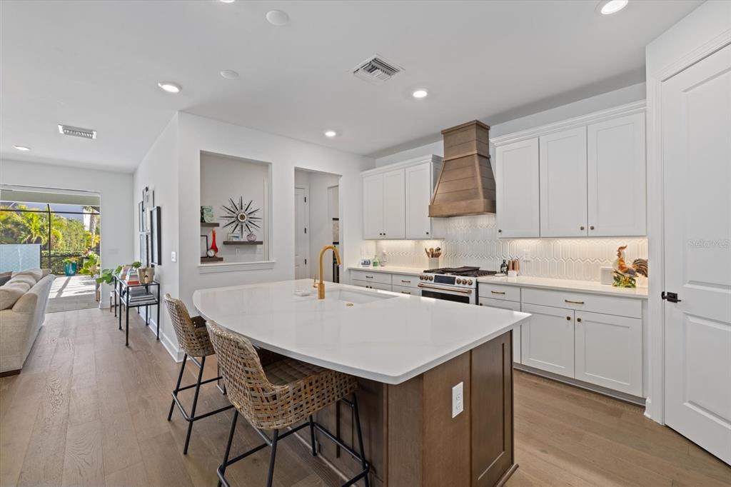 A modern kitchen features white cabinets, a wood range hood, and a large central island — 11712 GOLDEN BAY PLACE, BRADENTON, FL