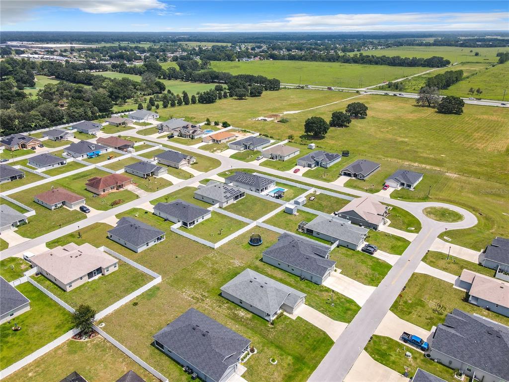 An aerial view shows a suburban neighborhood with single-family homes surrounded by open grassy fields — 5541 SE 92ND STREET, OCALA, FL