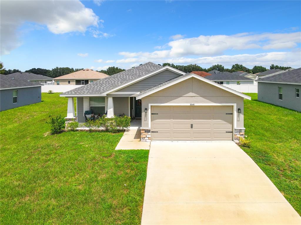 A single-story suburban house with a tan stucco exterior, a two-car garage, and a lawn — 5541 SE 92ND STREET, OCALA, FL
