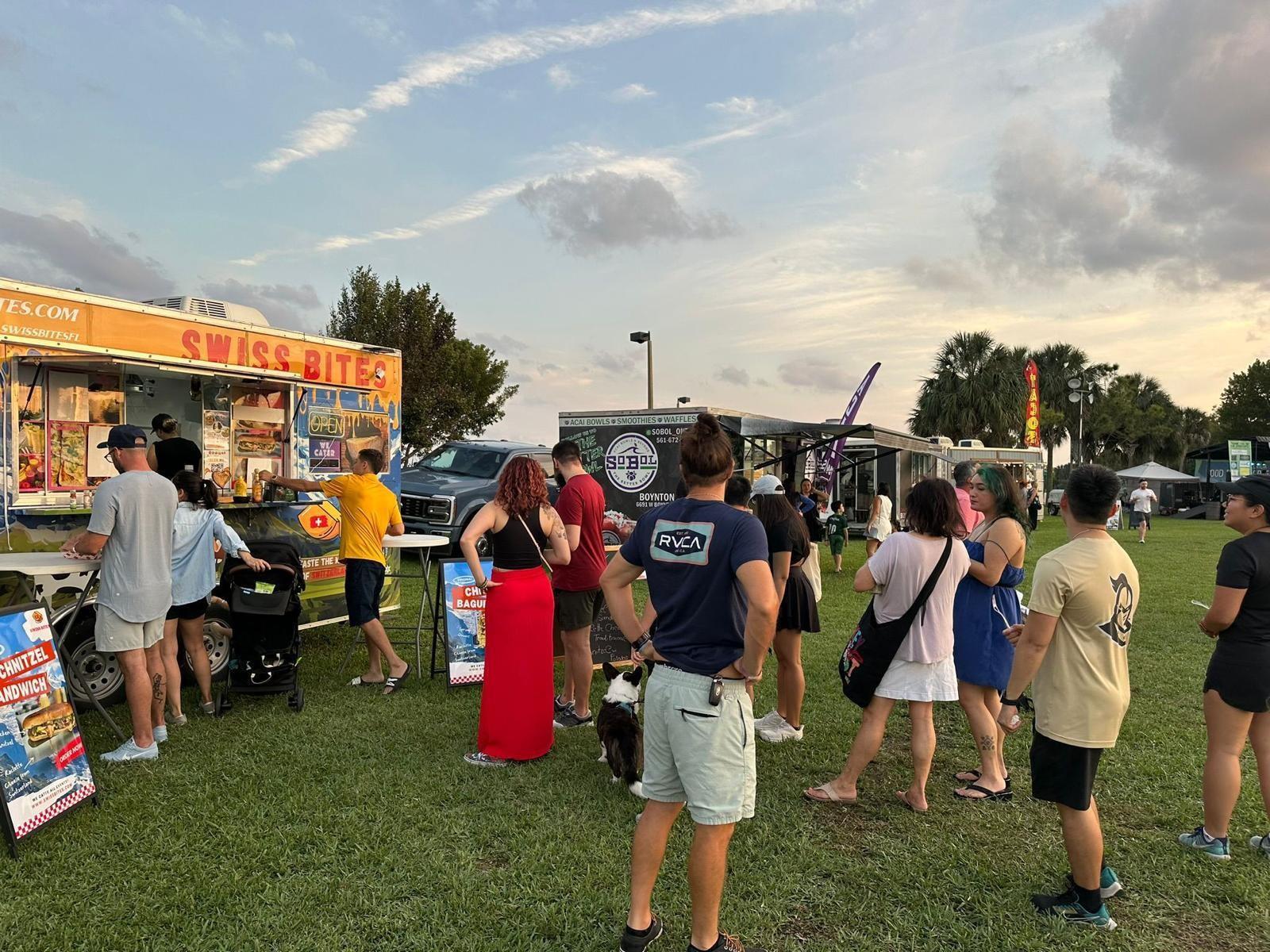 People stand in line at food trucks parked on a grassy field at sunset — Hollywood Avenue, Hollywood FL 33020, HOLLYWOOD, FL