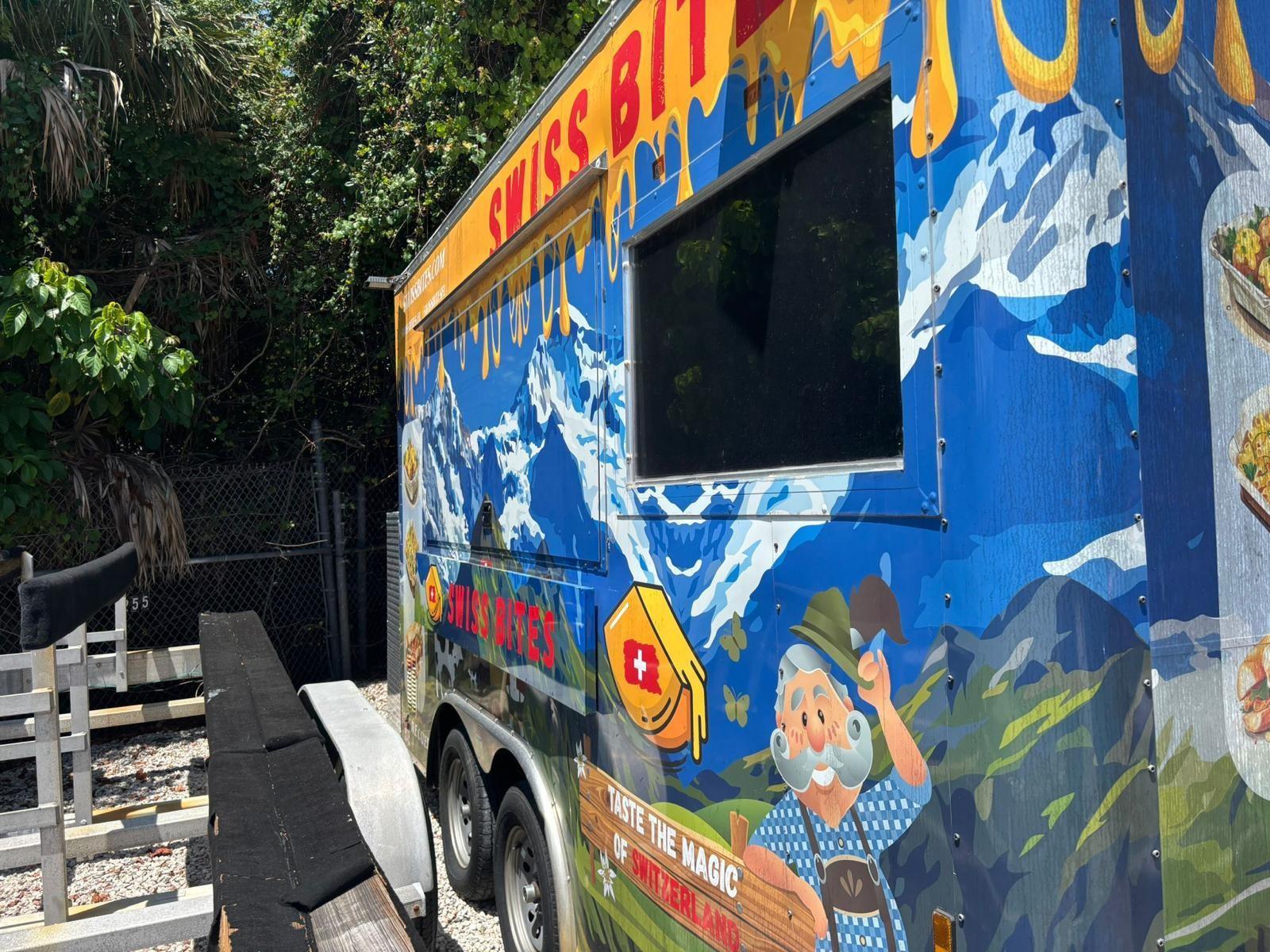 A food trailer with a Swiss-themed mural parked on a gravel lot next to a fence — Hollywood Avenue, Hollywood FL 33020, HOLLYWOOD, FL