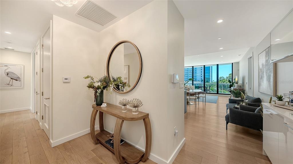 A modern entryway features a wooden console table, a round mirror, and light hardwood floors — 300 S PINEAPPLE AVENUE UNIT 302, SARASOTA, FL