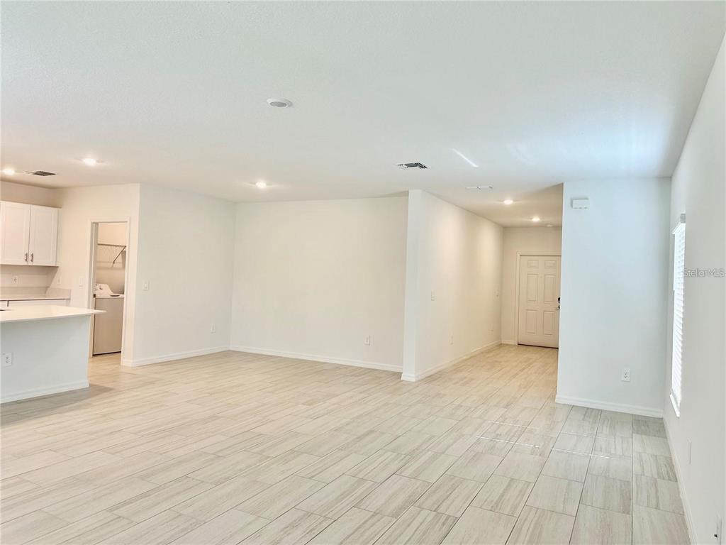 An open-concept living area features light-colored wood-look tile flooring and white walls — 17606 HAPPYTRAILS STREET, LAND O LAKES, FL