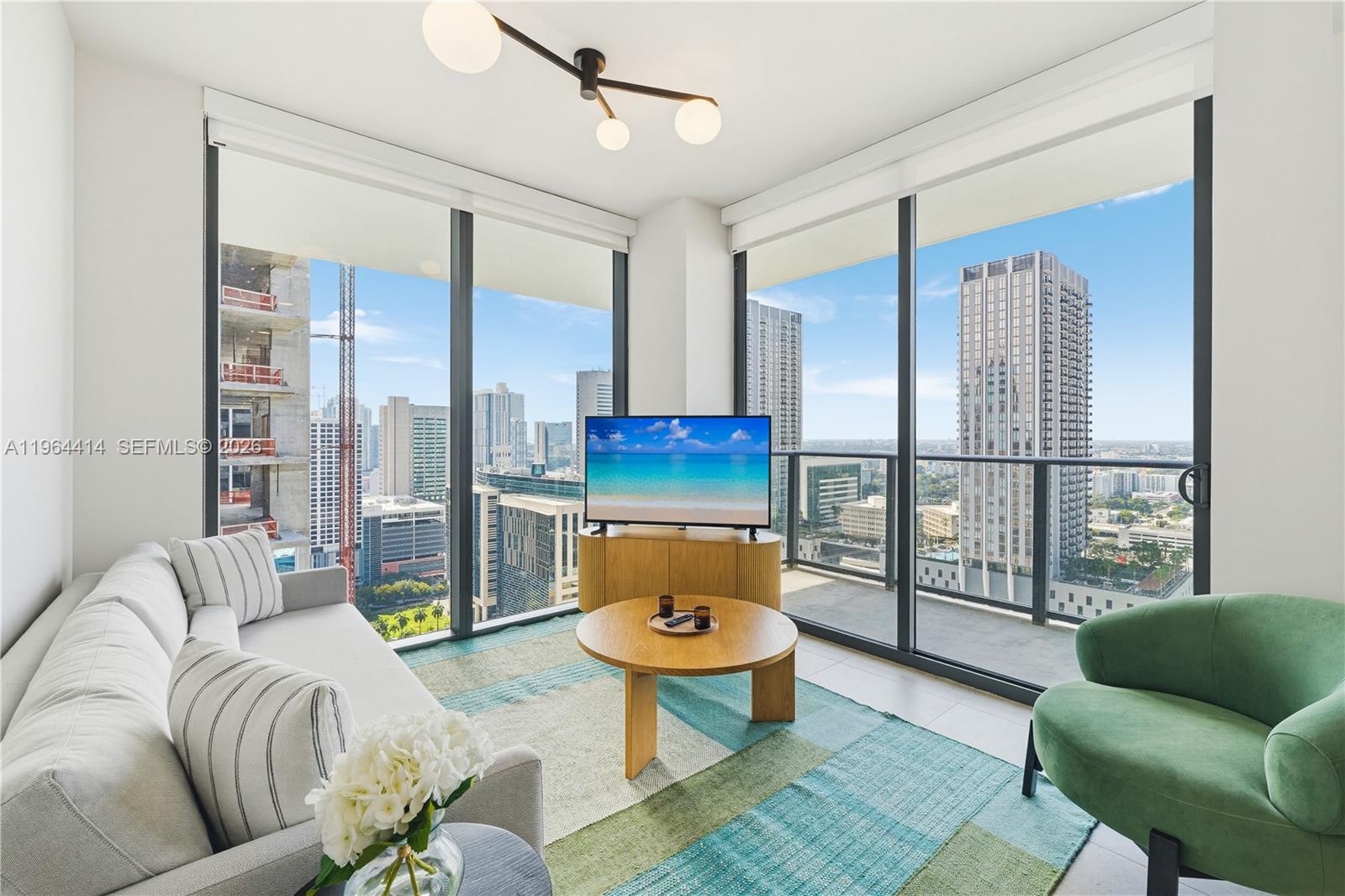 A modern living room features floor-to-ceiling windows, a light sofa, and a green armchair — 11 NE 6th # 2901, Miami FL 33132, MIAMI, FL