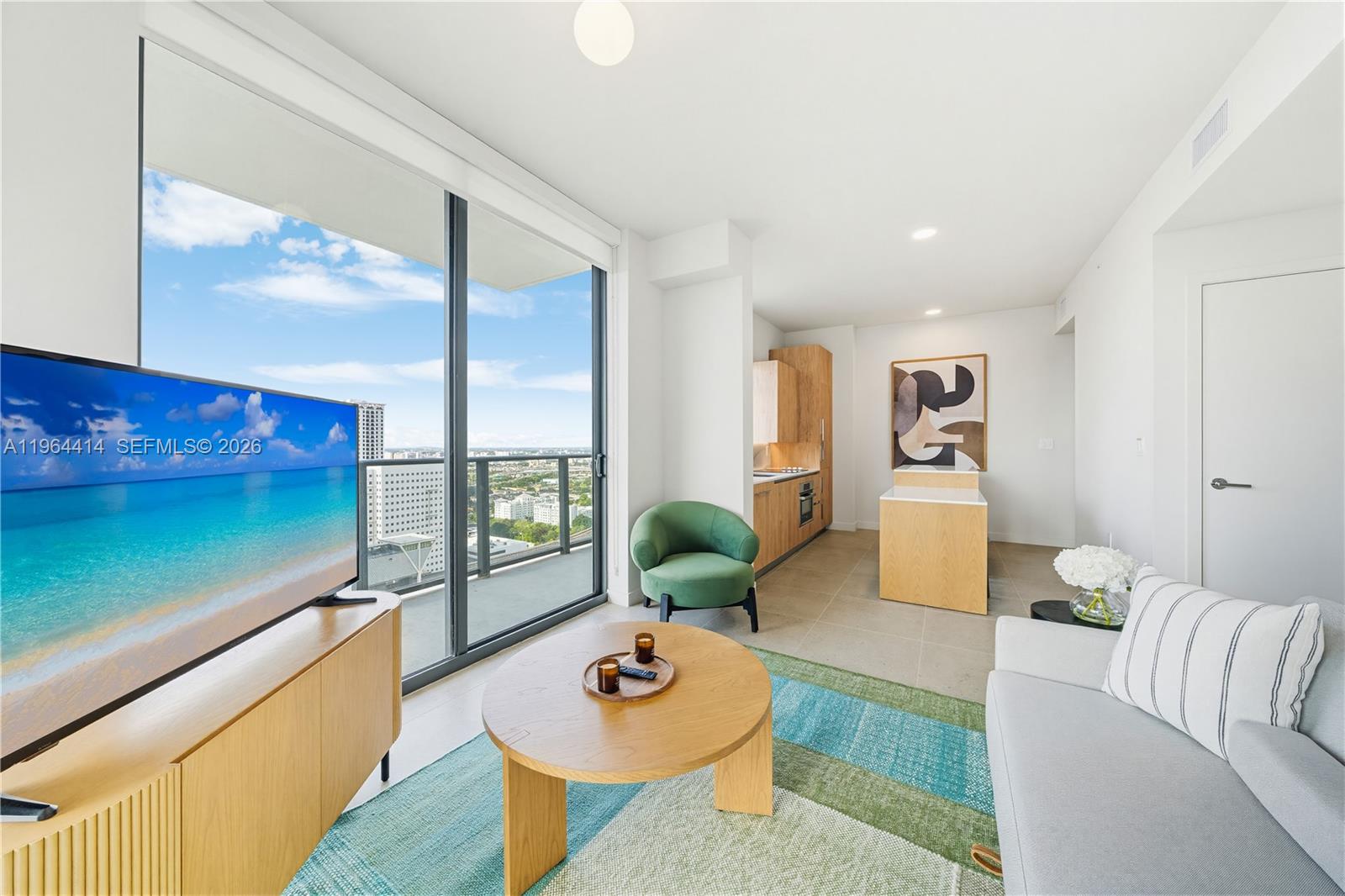 A modern living room features a light wood media console, a round coffee table, and a balcony — 11 NE 6th # 2901, Miami FL 33132, MIAMI, FL
