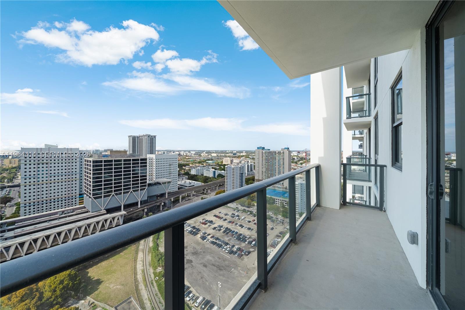 A high-rise balcony overlooks a parking lot, train tracks, and city buildings under a blue sky — 11 NE 6th # 2901, Miami FL 33132, MIAMI, FL