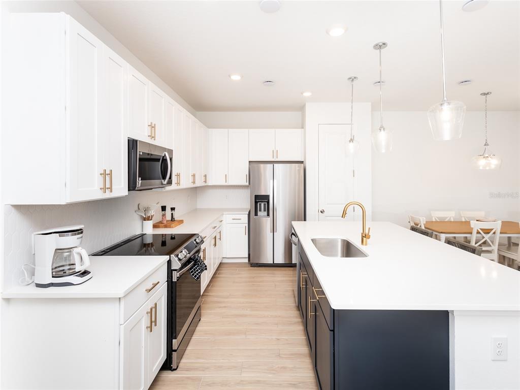 A modern kitchen features white upper cabinets, dark lower cabinets, a central island, and stainless appliances — 783 LONGBOAT DRIVE, DAVENPORT, FL