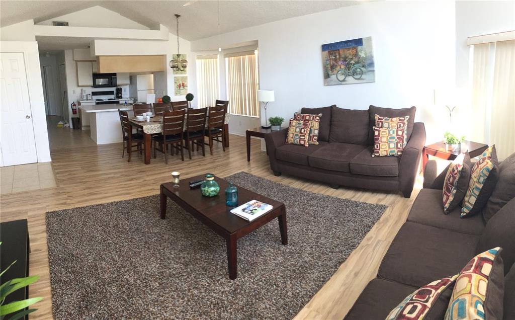 An open-concept living and dining area features wood-look flooring, brown sofas, and a kitchen — 2480 SWEETWATER CLUB CIRCLE UNIT 98, KISSIMMEE, FL
