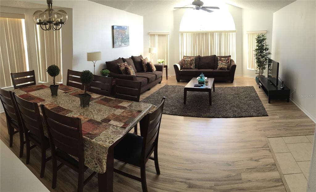 An open-concept living and dining area features wood-look flooring, dark furniture, and large windows — 2480 SWEETWATER CLUB CIRCLE UNIT 98, KISSIMMEE, FL
