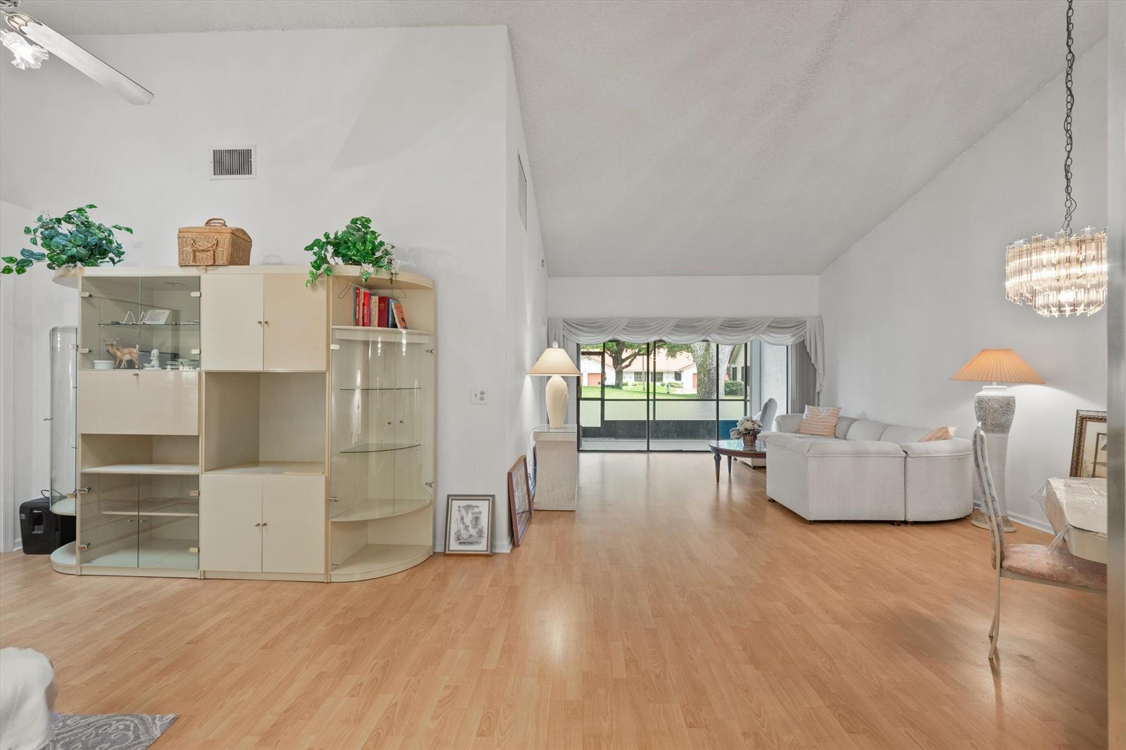 A living room with light wood flooring, vaulted ceilings, a large wall unit, and sliding doors — 9832 Pavarotti Terrace # 103, Boynton Beach FL 33437, BOYNTON BEACH, FL