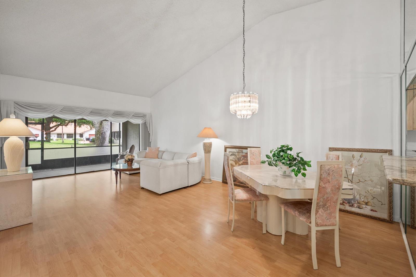 A living and dining area with light wood flooring, vaulted ceilings, and a sliding glass door — 9832 Pavarotti Terrace # 103, Boynton Beach FL 33437, BOYNTON BEACH, FL