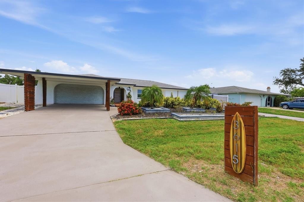 A single-story house with a carport and a surfboard-shaped address sign in the front yard — 3615 EGERTON CIRCLE, SARASOTA, FL