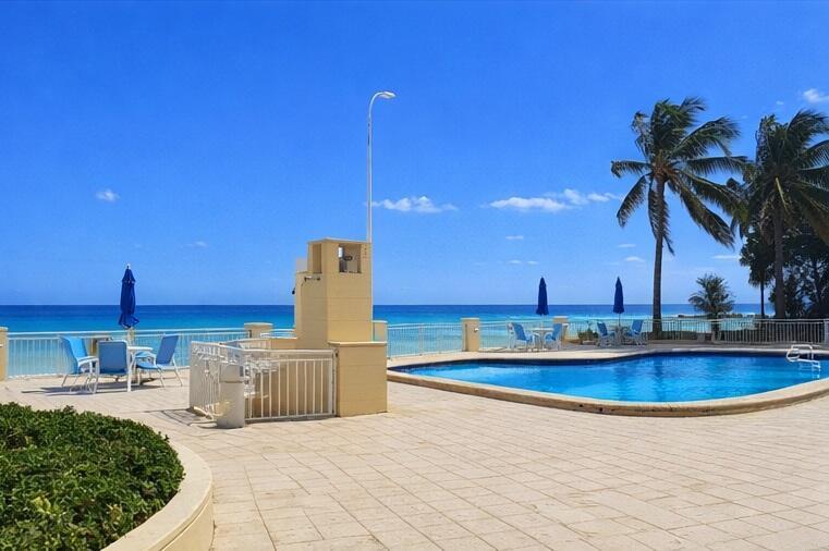 A swimming pool sits on a tiled patio overlooking the ocean with palm trees nearby — 3475 S Ocean Boulevard # 3020, Palm Beach FL 33480, PALM BEACH, FL
