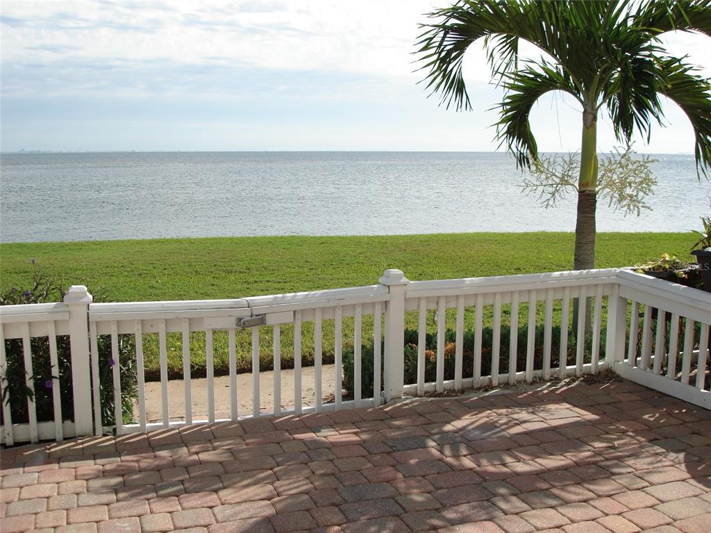 A brick patio overlooks a grassy lawn and the ocean behind a white picket fence — 5248 BEACH DRIVE SE UNIT 5248, ST PETERSBURG, FL