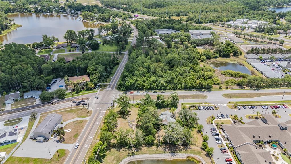 An aerial view shows a road intersection, commercial buildings, and surrounding wooded areas with ponds — 18950 SUNLAKE BOULEVARD, LUTZ, FL
