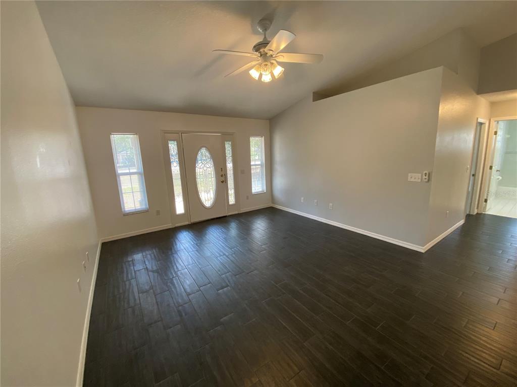 An empty living room features dark wood-look tile flooring, a ceiling fan, and a front door — 9195 SE 163RD STREET, SUMMERFIELD, FL