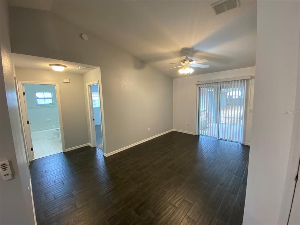 An empty room features dark wood-look tile flooring, a ceiling fan, and sliding glass doors — 9195 SE 163RD STREET, SUMMERFIELD, FL