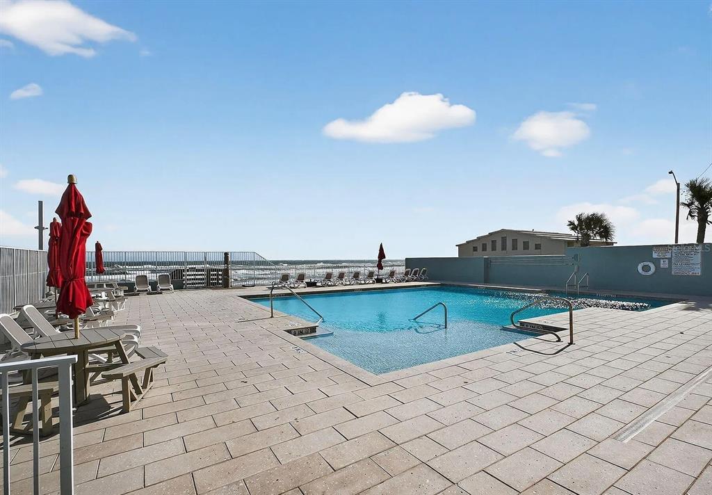 A swimming pool with lounge chairs and umbrellas overlooks the ocean from a paved deck — 800 N ATLANTIC AVENUE UNIT 420, DAYTONA BEACH, FL