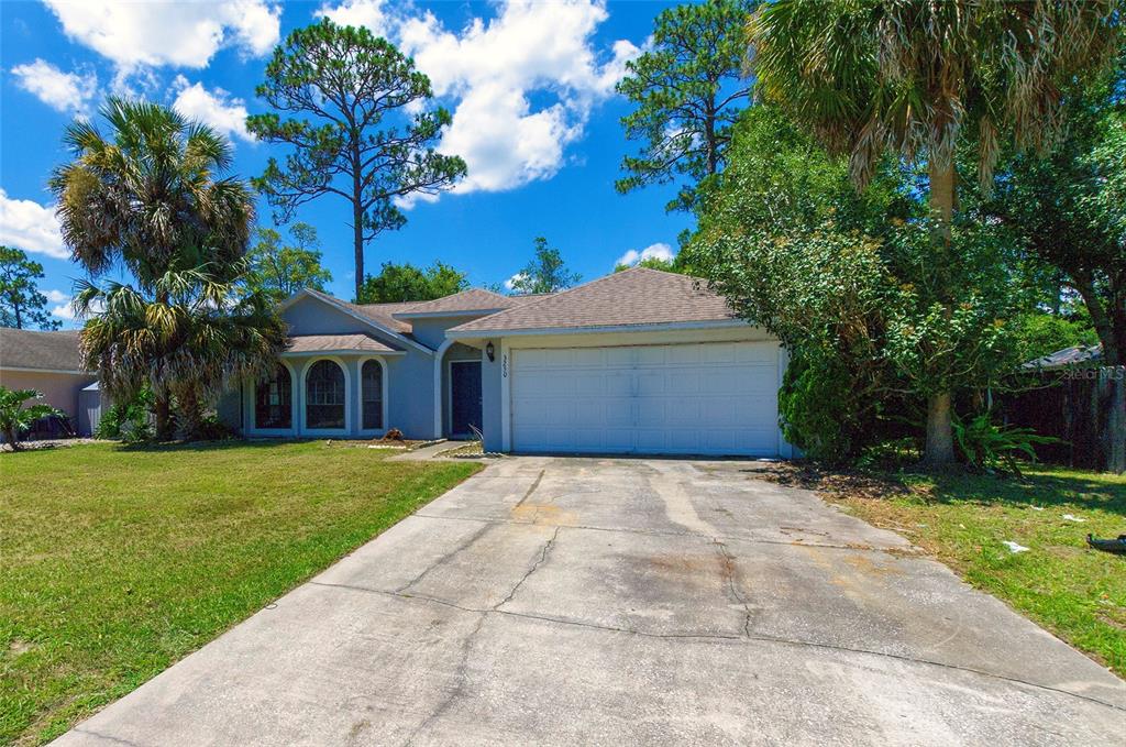 A single-story house with a white garage door and a concrete driveway sits under trees — 3250 CLEWISTON STREET, DELTONA, FL