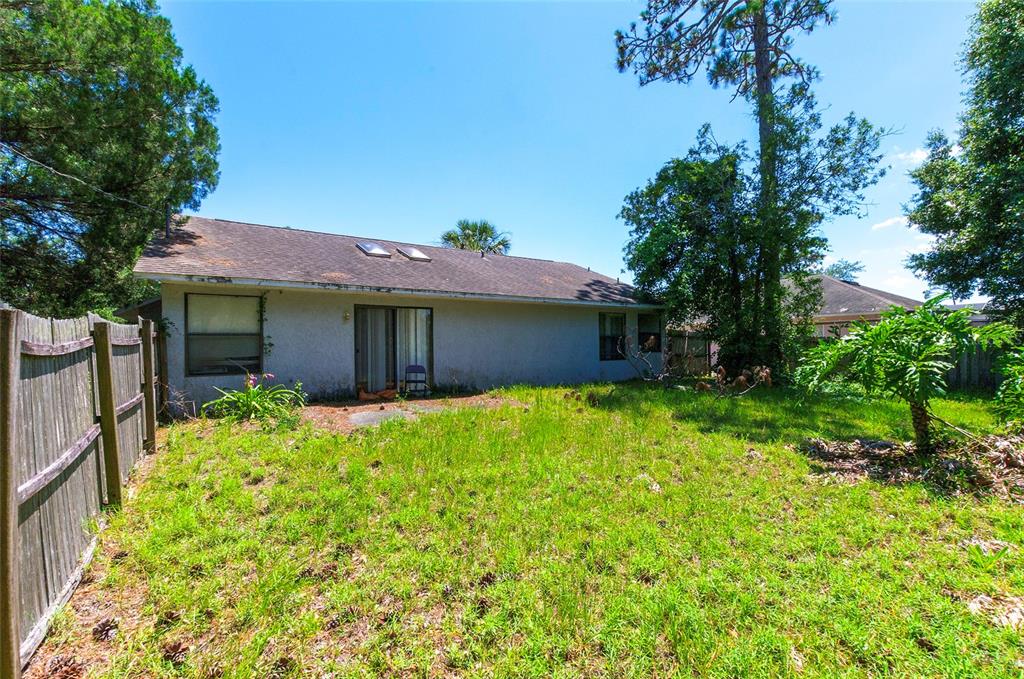 The exterior view shows the back of a house with a yard and wooden fence — 3250 CLEWISTON STREET, DELTONA, FL