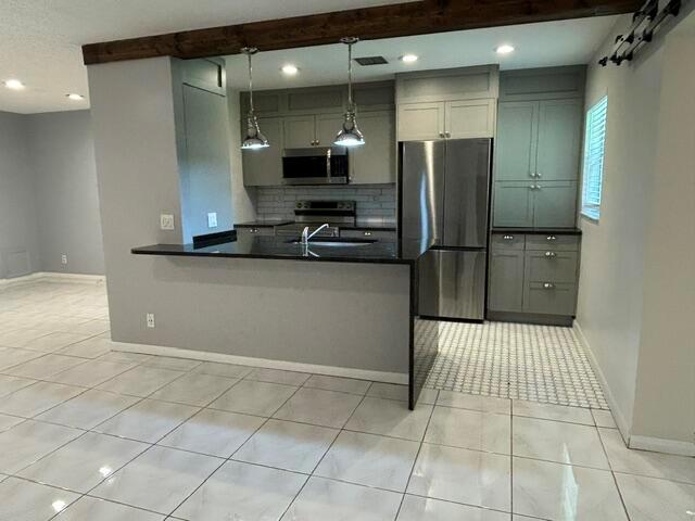 A kitchen features gray cabinets, stainless steel appliances, a breakfast bar, and light-colored tile flooring — 5270 Nesting Way # B, Delray Beach FL 33484, DELRAY BEACH, FL