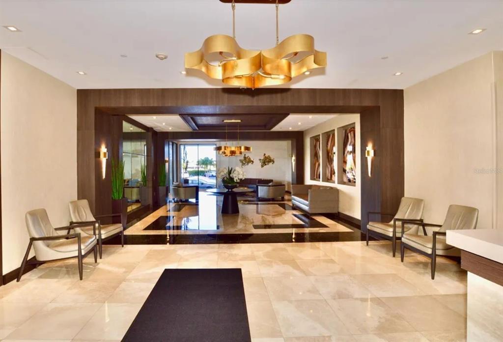 A modern building lobby features a gold chandelier, marble floors, and seating areas — 20505 E COUNTRY CLUB DRIVE UNIT 534, MIAMI, FL