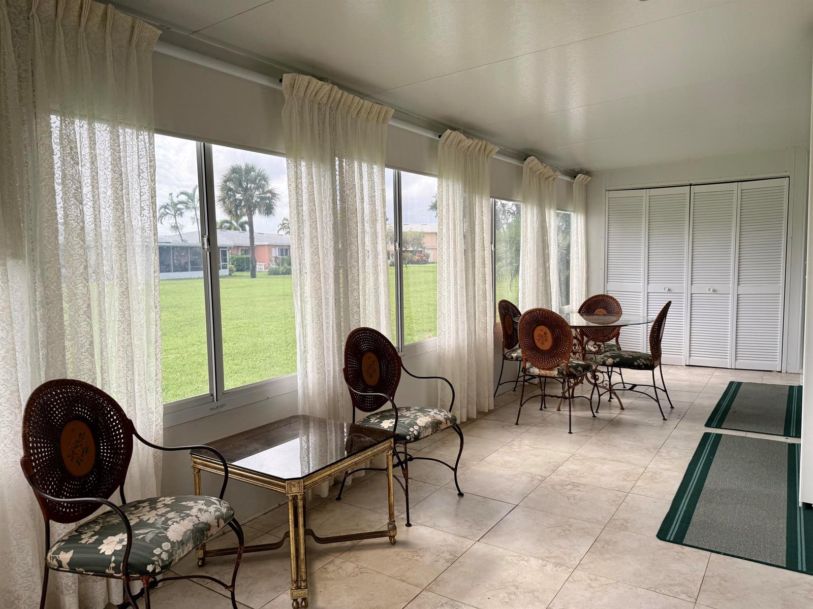 A sunroom features tile flooring, large windows with lace curtains, and a dining set — 1460 NW 19th Terrace # a, Delray Beach FL 33445, DELRAY BEACH, FL