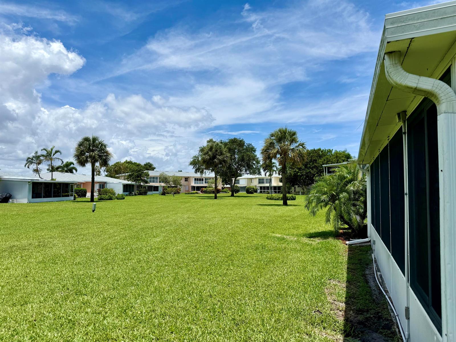 A grassy lawn sits between residential buildings under a blue sky with scattered clouds — 1460 NW 19th Terrace # a, Delray Beach FL 33445, DELRAY BEACH, FL