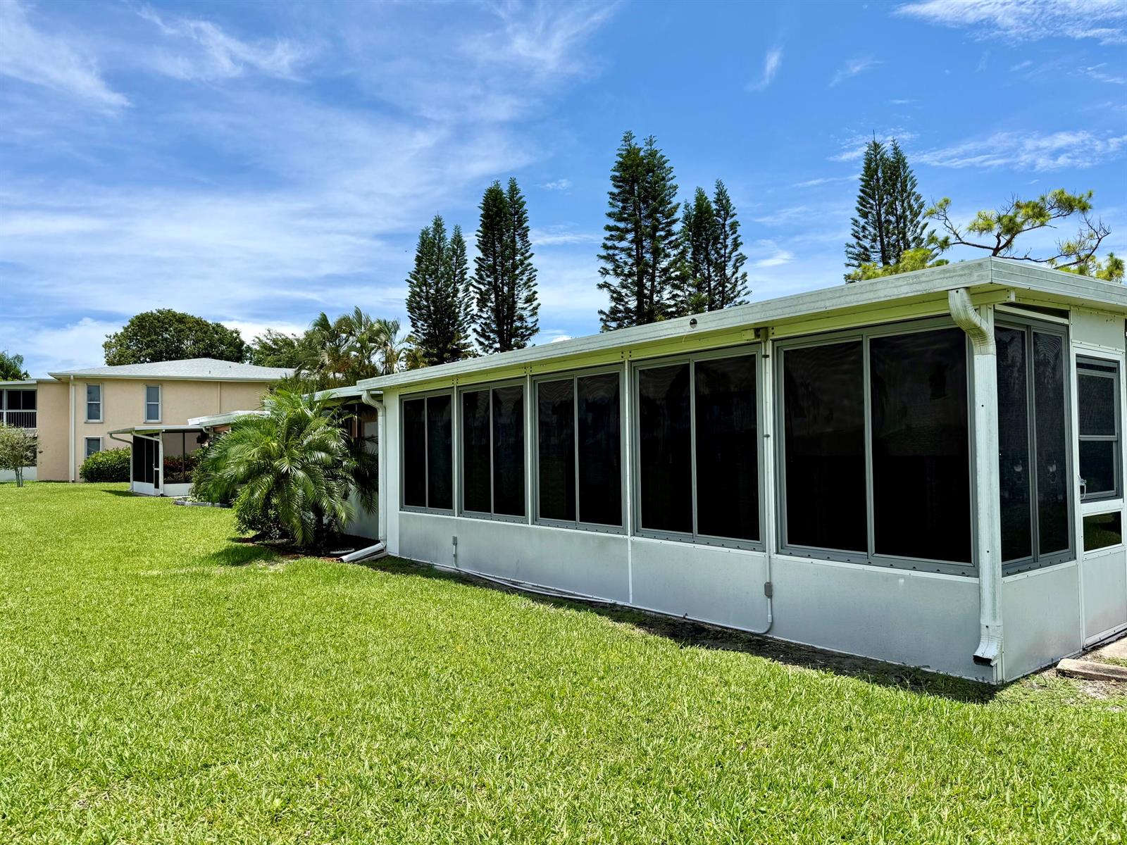 A white sunroom with large windows sits on a grassy lawn near tall trees — 1460 NW 19th Terrace # a, Delray Beach FL 33445, DELRAY BEACH, FL