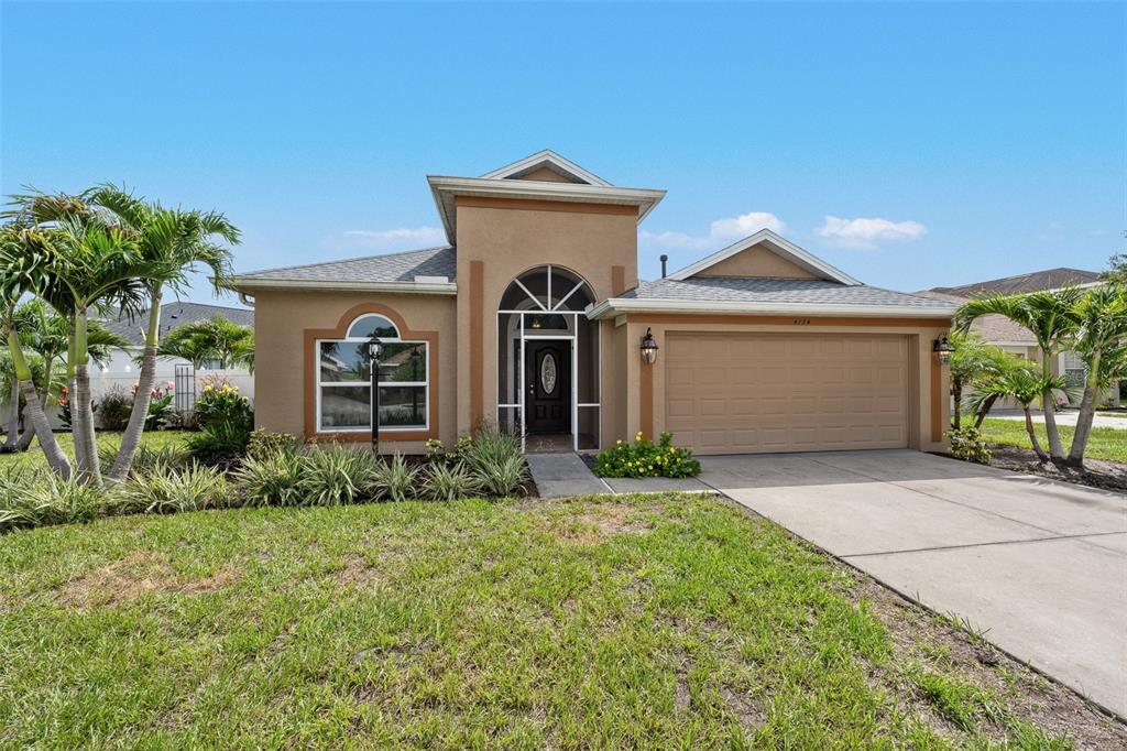 A single-story tan stucco house features a prominent arched entryway and a two-car garage — 4124 101ST AVENUE E, PARRISH, FL