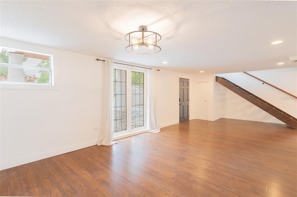 A room with wood-look flooring, a modern light fixture, glass doors, and a wooden staircase — 206 W FRIERSON AVENUE, TAMPA, FL