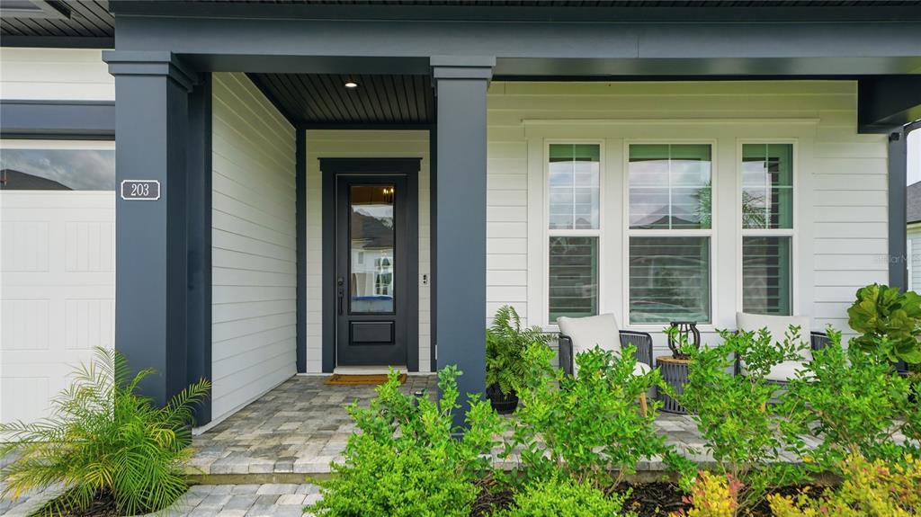 A covered front porch features a dark door, white siding, and a paver walkway — 203 TESORO TERRACE, ST AUGUSTINE, FL